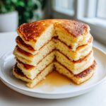 A tall stack of fluffy pancakes, cut to show the airy interior, drizzled with syrup.