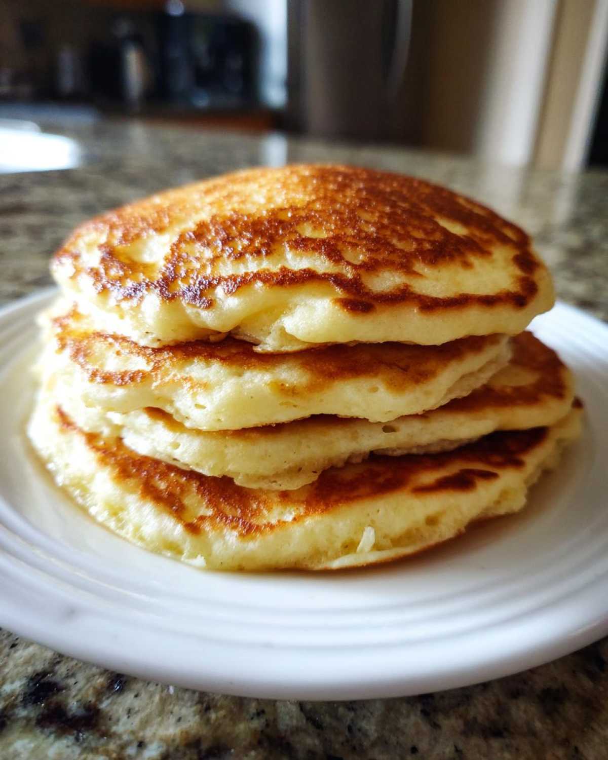 A tall stack of four fluffy pancakes with perfectly golden brown tops and edges, served on a white plate.