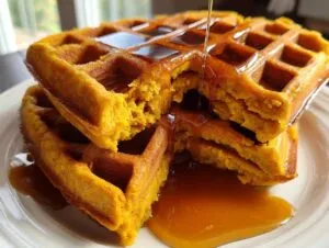Close-up of a stack of fluffy pumpkin waffles being drizzled with maple syrup.
