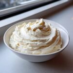 A close-up of fluffy vanilla buttercream frosting swirled high in a white bowl, ready for use.