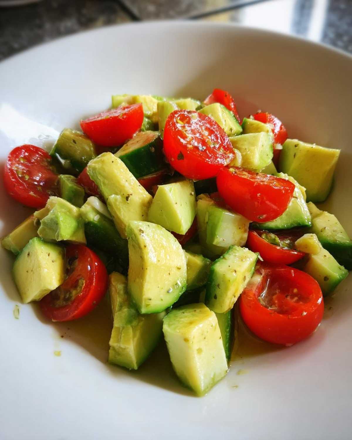 Close-up of chunky avocado salad mixed with halved cherry tomatoes and a light dressing in a white bowl.
