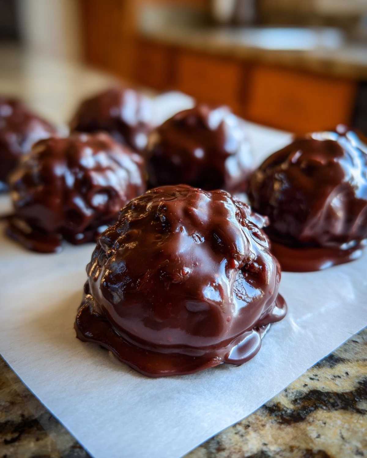Close-up of several freshly made chocolate covered cherries resting on white parchment paper.