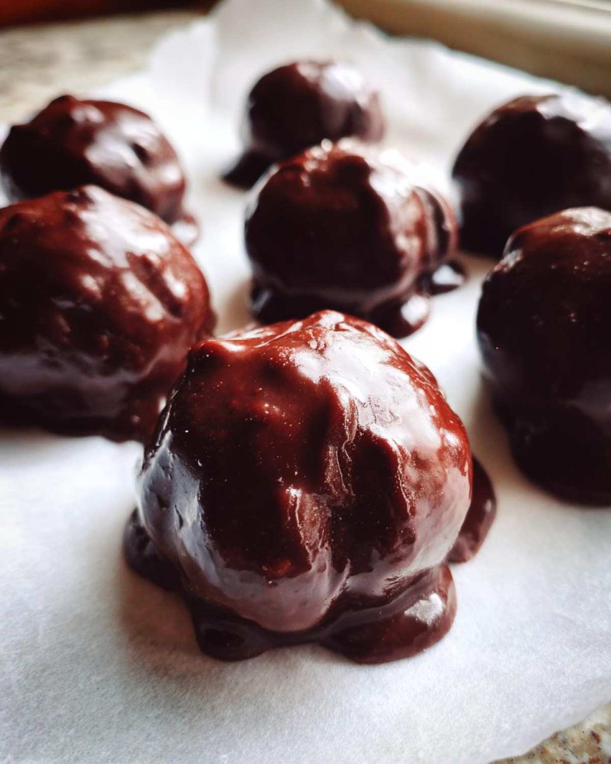 Close-up of several freshly made chocolate covered cherries resting on white parchment paper.