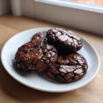 Four fudgy chocolate brownie cookies topped with flaky sea salt on a white plate.