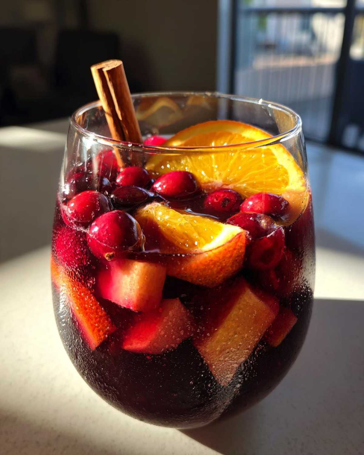 Close-up of a glass filled with cold Christmas sangria, loaded with cranberries, orange slices, and a cinnamon stick.