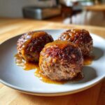 Three perfectly formed mini meatloaf portions covered in a rich, shiny glaze, served on a light gray plate.