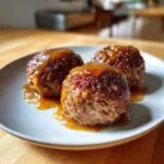 Three perfectly formed mini meatloaf portions covered in a rich, shiny glaze, served on a light gray plate.