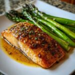 A perfectly cooked salmon recipe fillet glazed with a savory sauce, served next to bright green roasted asparagus.