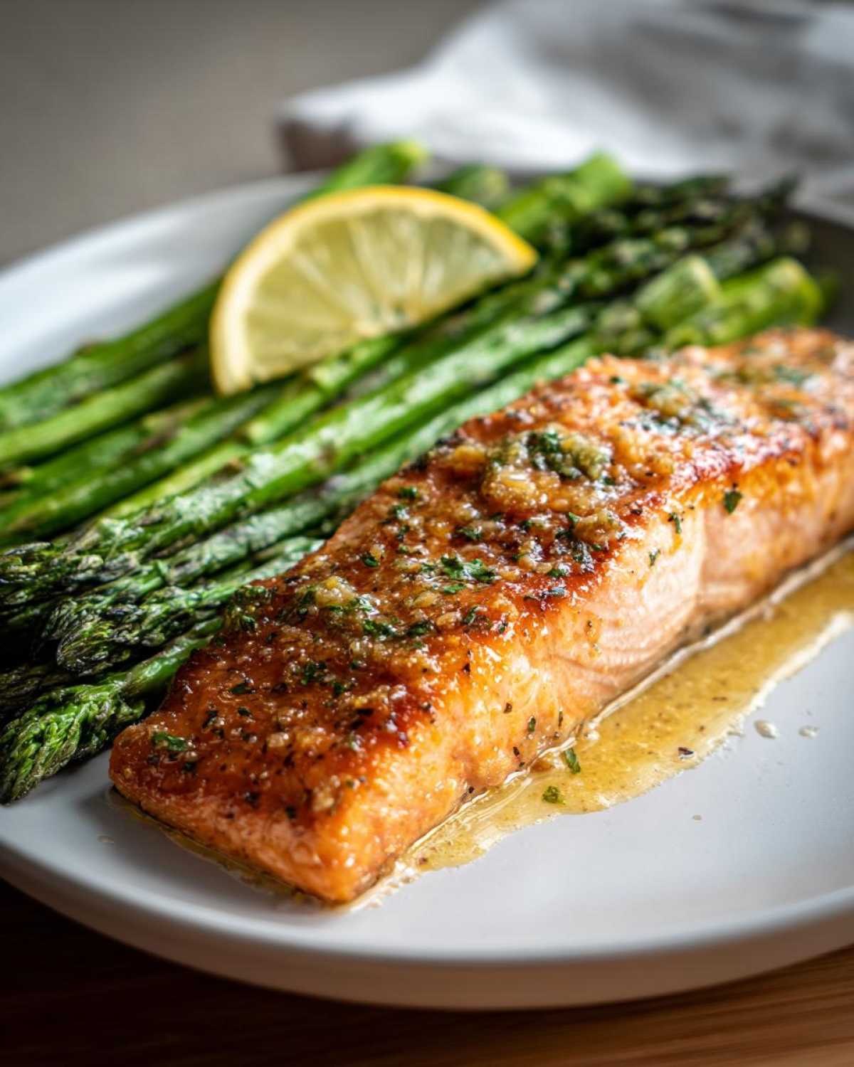 Close-up of a perfectly cooked salmon recipe fillet glazed with garlic butter, served alongside bright green asparagus and a lemon wedge.