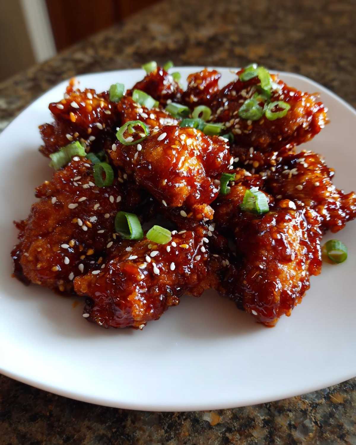 Close-up of crispy gochujang chicken pieces coated in a sticky, dark red glaze, topped with sesame seeds and chopped green onions.