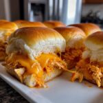 Close-up of gooey, melted cheese dripping over shredded chicken filling in freshly baked buffalo chicken sliders.