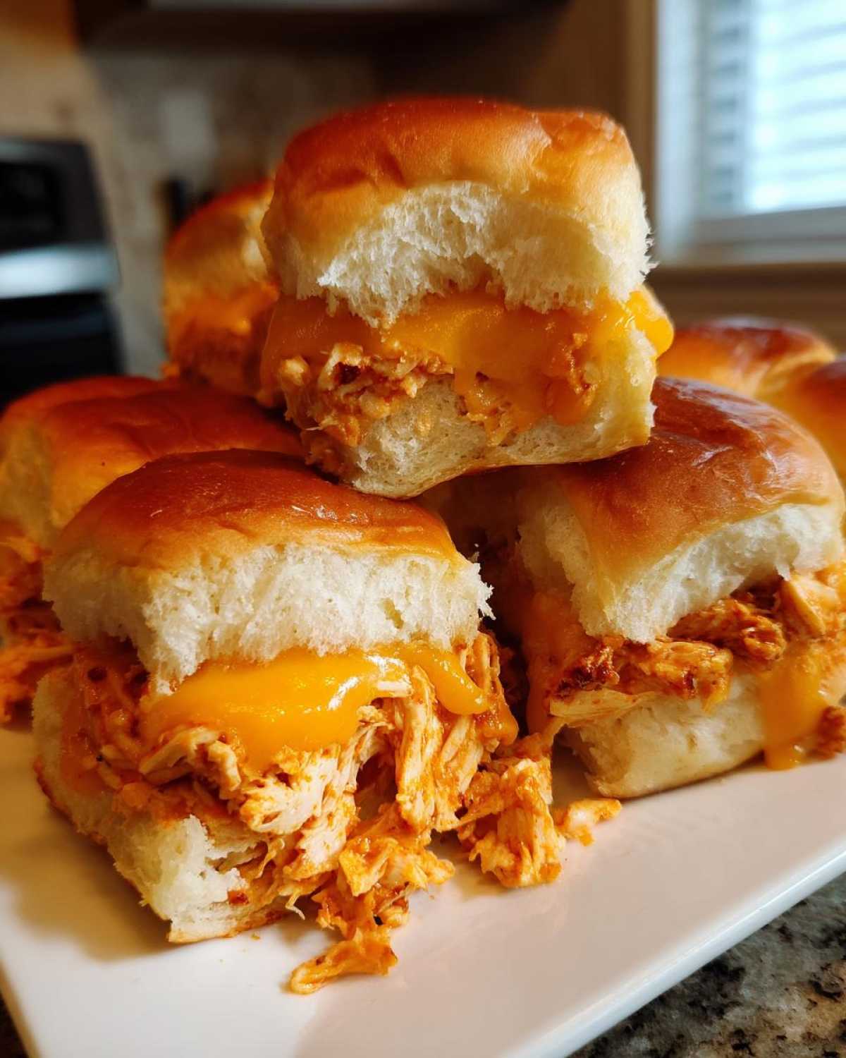 A stack of gooey buffalo chicken sliders featuring shredded chicken and melted cheddar cheese on soft rolls.