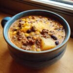 Close-up of a steaming bowl of rich cowboy soup featuring ground beef, corn, beans, potatoes, and melted cheese.