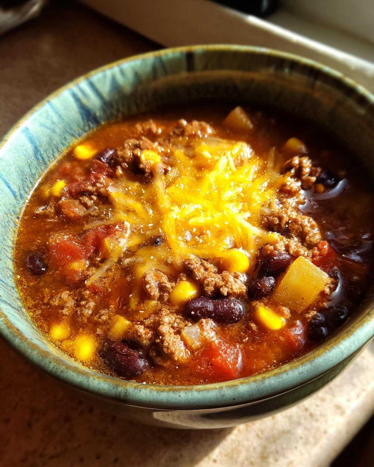 Close-up of a steaming bowl of cowboy soup featuring ground beef, beans, corn, and melted cheddar cheese.
