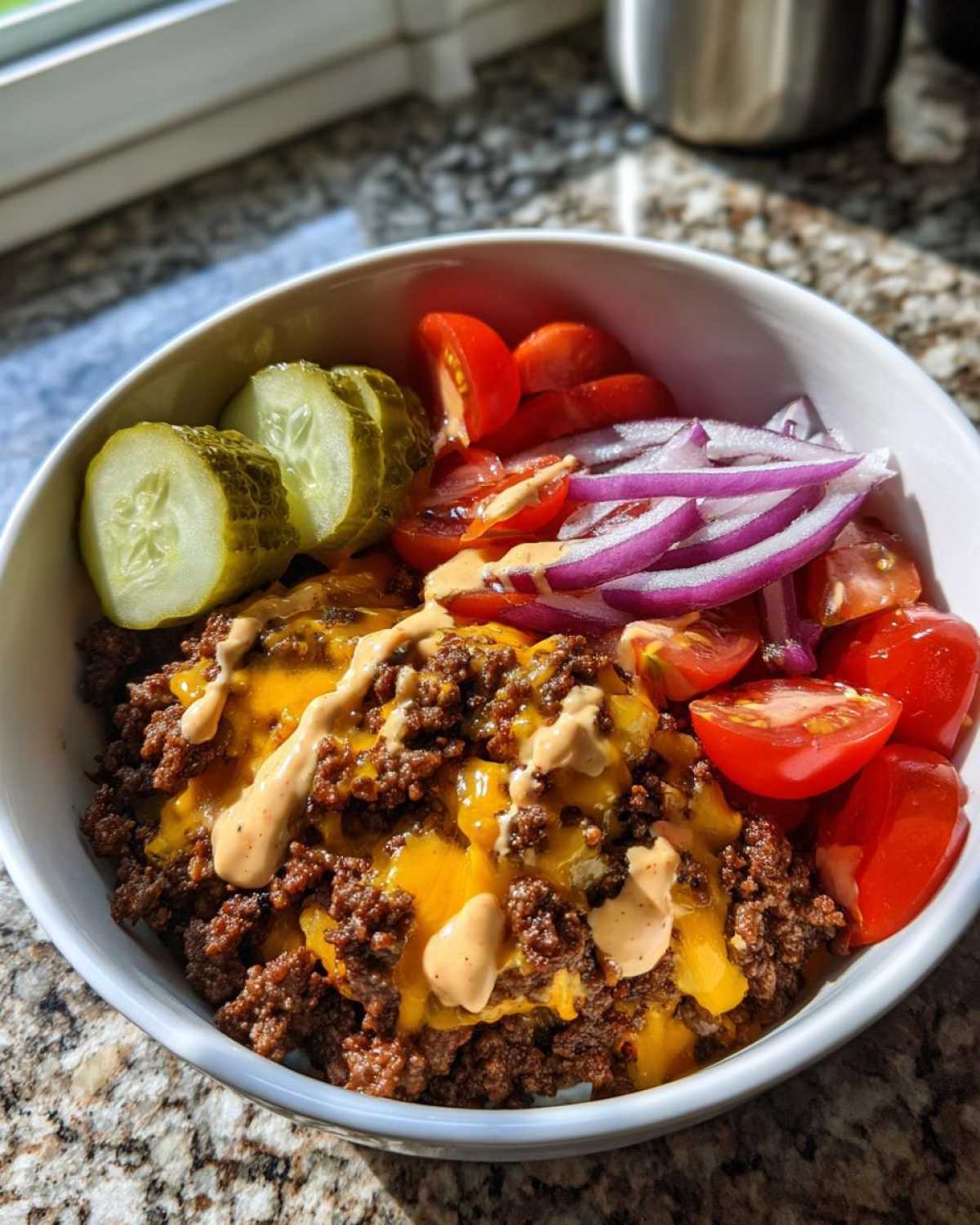 Close-up of a high-protein cheeseburger bowl featuring seasoned ground beef, melted cheese, pickles, tomatoes, and onions.