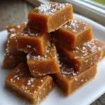 A stack of rich, chewy squares of homemade caramel topped with flaky sea salt.
