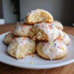 A stack of soft Italian ricotta cookies topped with white glaze and colorful sprinkles, one cookie is broken open.