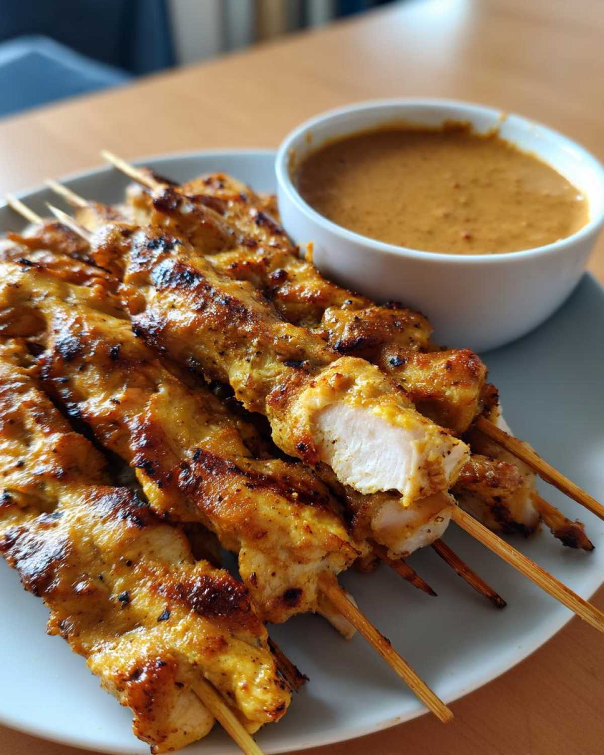 Close-up of grilled chicken satay skewers on a plate next to a bowl of peanut dipping sauce.