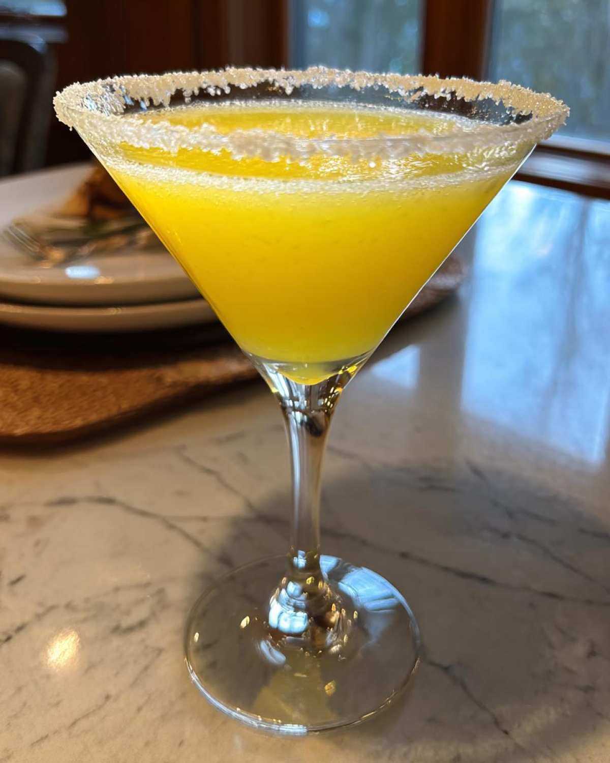 A vibrant, yellow lemon drop martini served in a stemmed glass with a thick sugar rim.