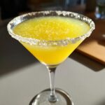 A vibrant yellow lemon drop martini served in a coupe glass with a thick, sparkling sugar rim.