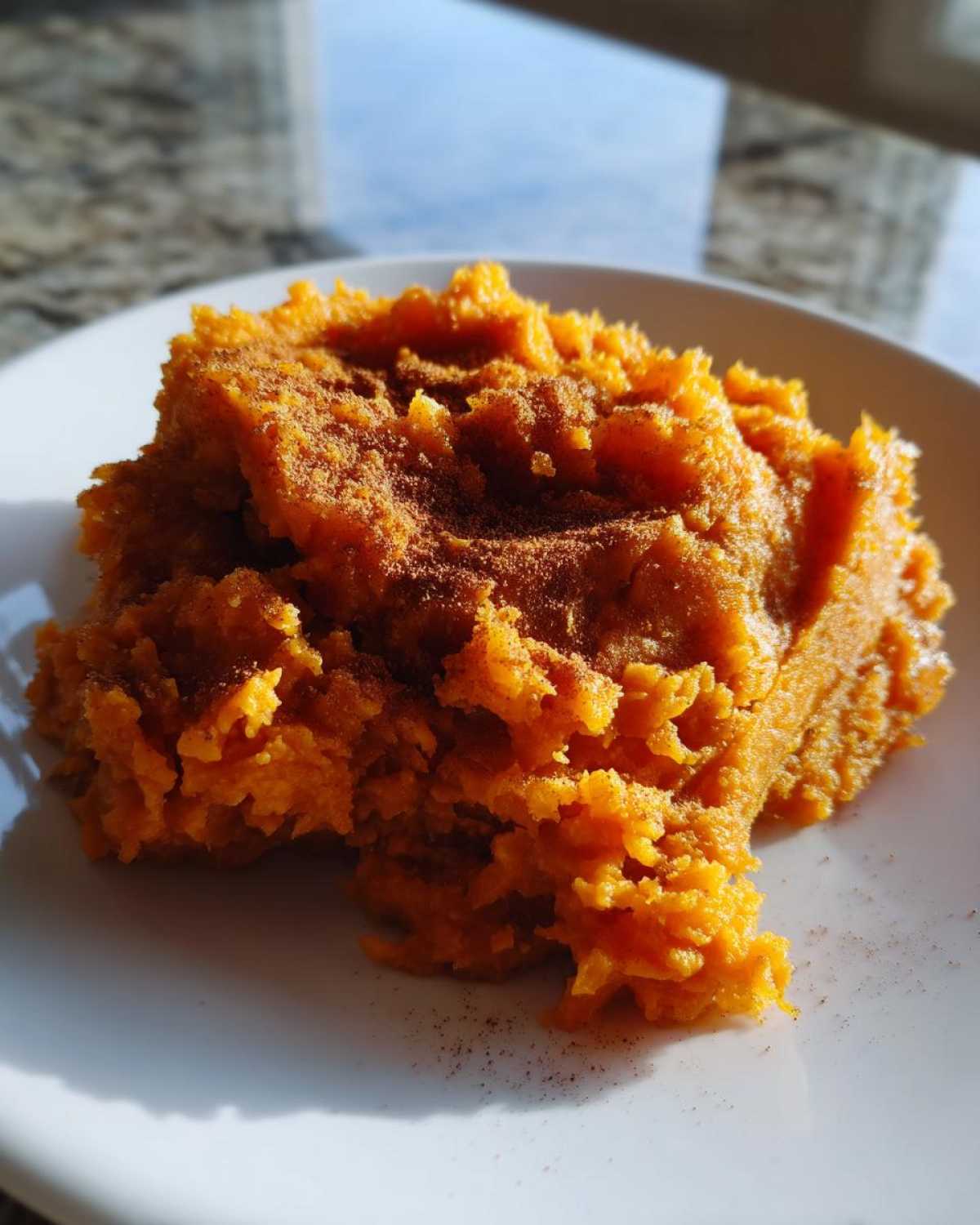 A close-up of bright orange mashed sweet potatoes topped with a dusting of cinnamon on a white plate.