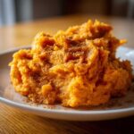 A close-up of fluffy, bright orange mashed sweet potatoes topped generously with ground cinnamon.
