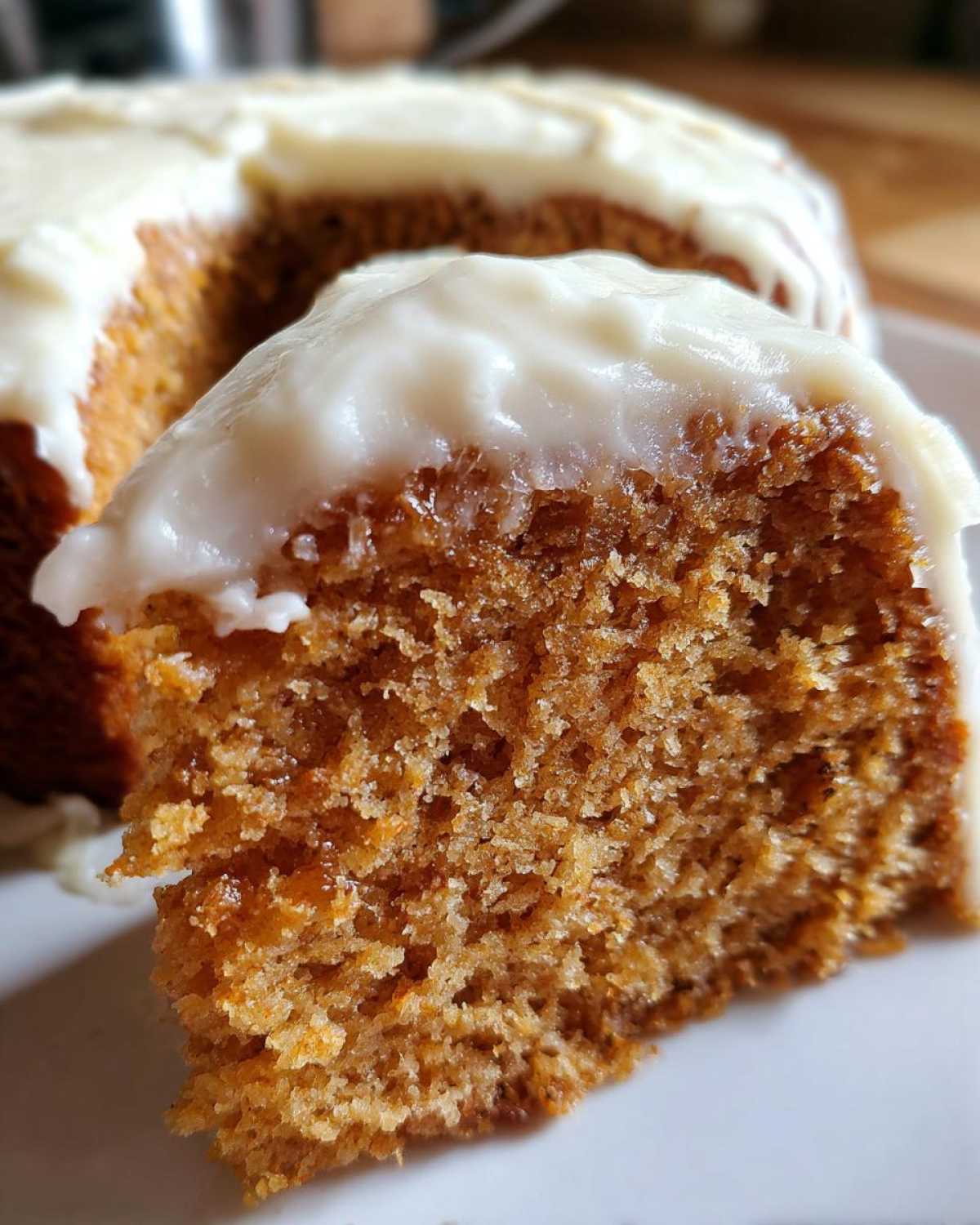 Close-up of a slice of super moist spice cake showing its crumb texture and thick cream cheese frosting.