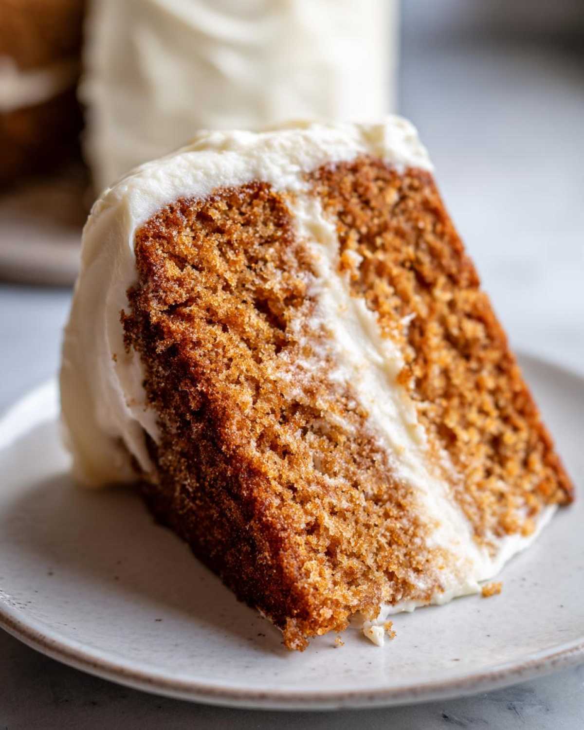 Close-up of a moist slice of spice cake layered with thick cream cheese frosting.