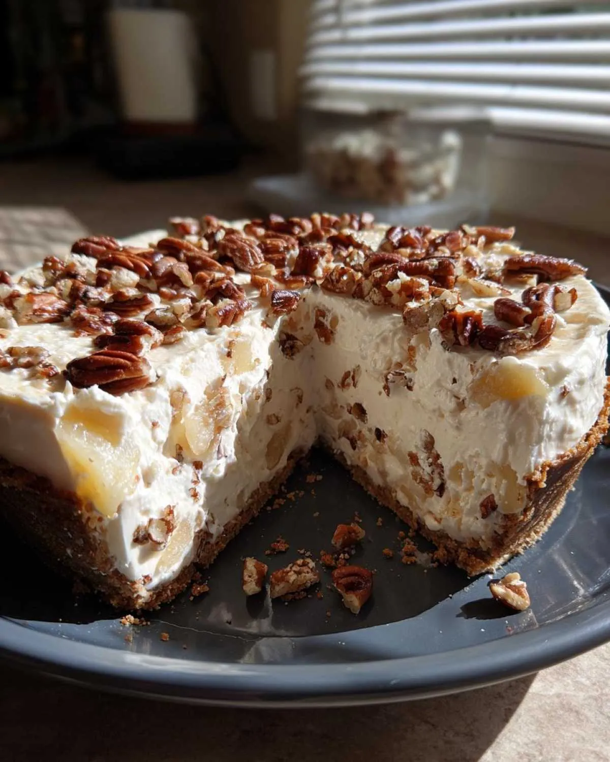 A close-up of a no-bake Million Dollar Pie with a slice removed, showing the creamy filling and pecan topping.
