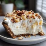 A thick slice of creamy no-bake Million Dollar Pie with a graham cracker crust, topped with whipped cream, pineapple chunks, and pecans.