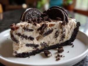A generous slice of no bake oreo pie featuring a dark crust, creamy filling loaded with cookie pieces, and topped with whole cookies.