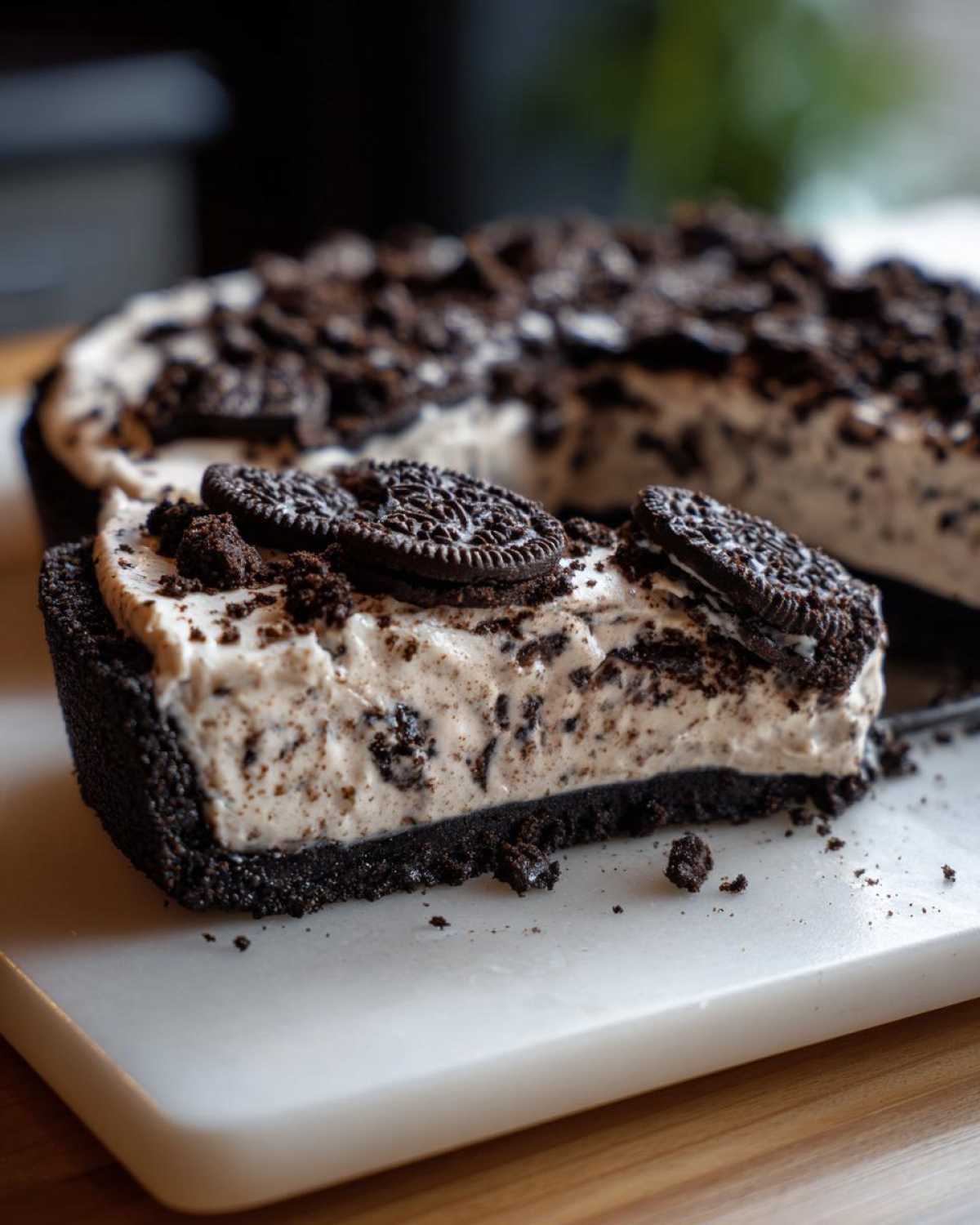 A close-up slice of a creamy no bake oreo pie showing the dark crust and cookie pieces in the filling, topped with whole cookies.