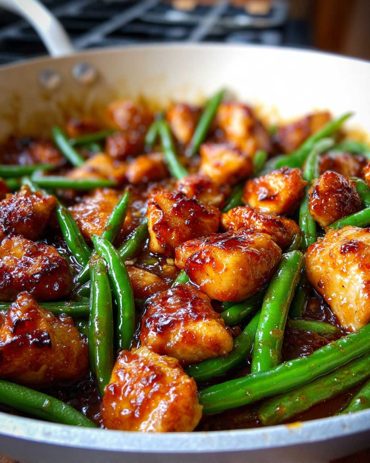 Close-up of glazed chicken pieces mixed with bright green beans in a white skillet, showing the amazing chicken and green beans dinner.