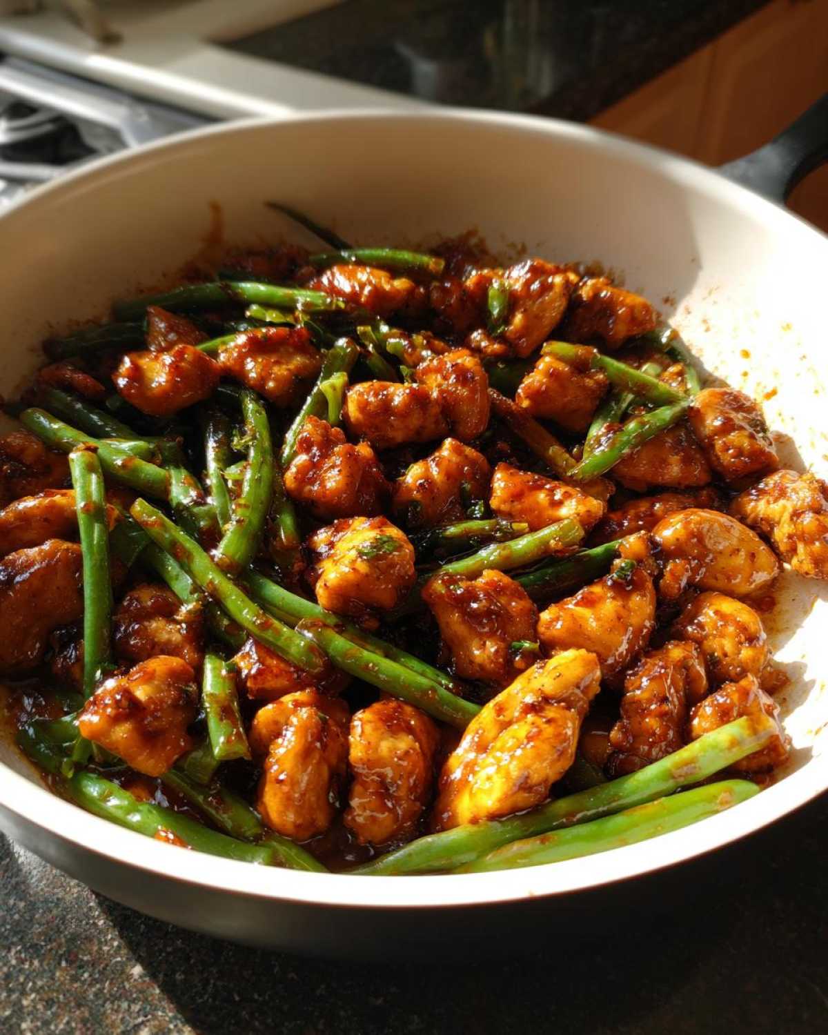 Close-up of glazed chicken and green beans mixed together in a white skillet, showcasing the amazing chicken and green beans dinner.