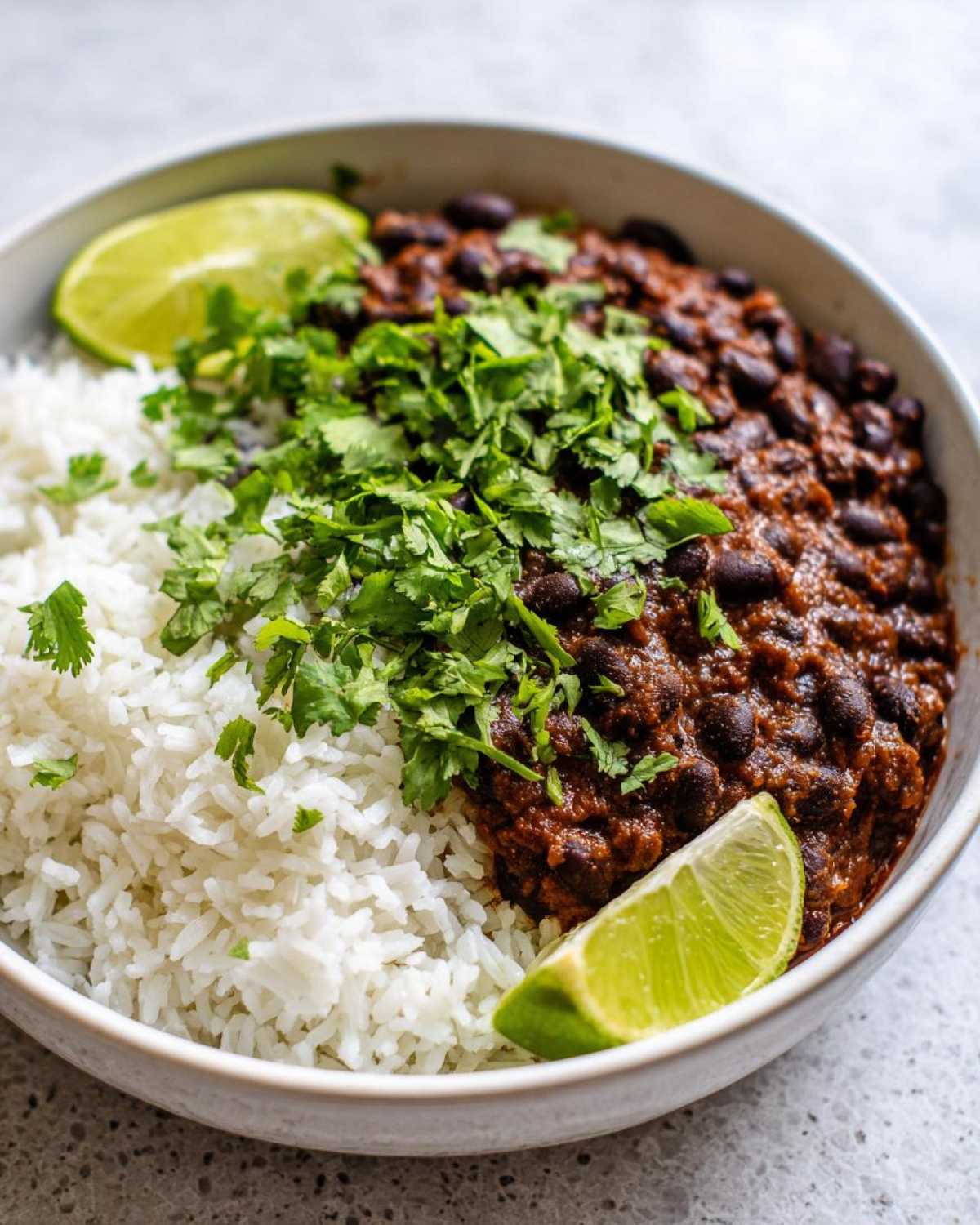 Close-up of a bowl of flavorful beans and rice topped with fresh cilantro and lime wedges.