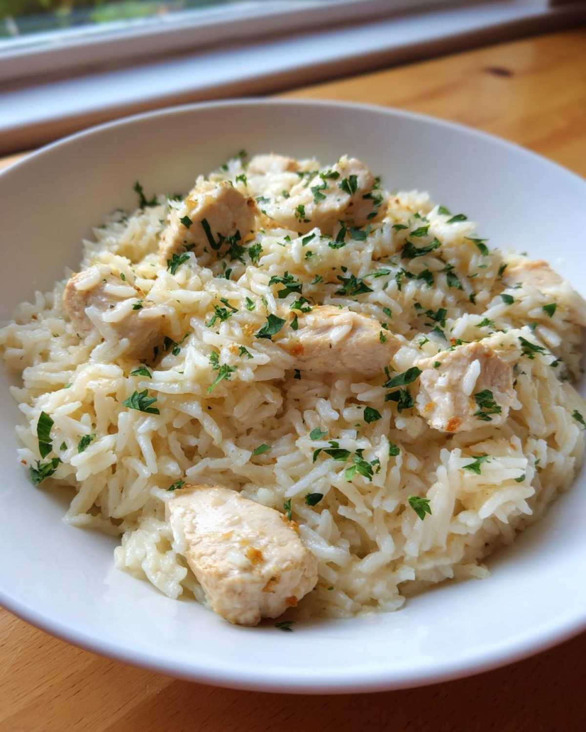 Close-up of a white bowl filled with creamy one pot chicken and rice, topped with fresh parsley.
