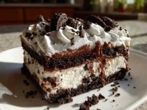 A decadent slice of layered ice cream cake featuring dark chocolate cake, white creamy filling, and whipped topping with cookie crumbles.