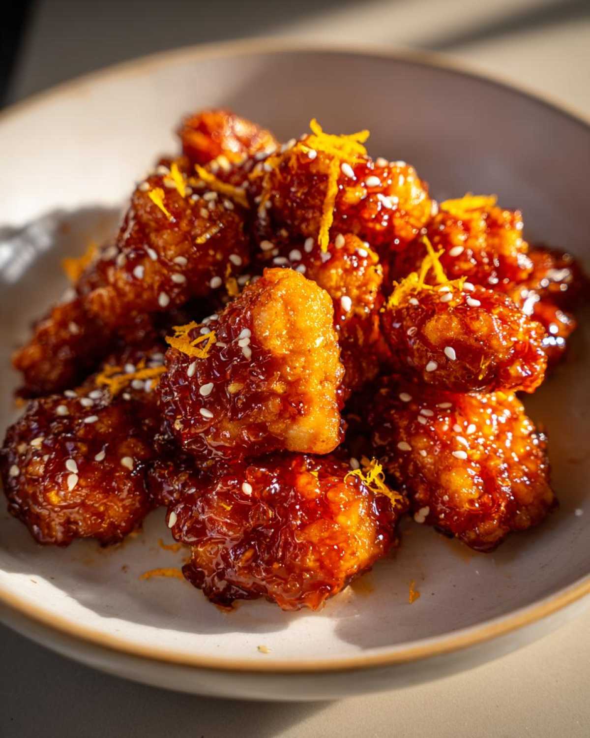 Close-up of crispy chicken pieces coated in a glossy sauce, garnished with sesame seeds and orange zest for the orange chicken recipe.