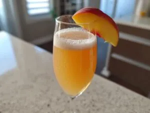 A sparkling, orange-hued bellini recipe cocktail served in a flute glass, garnished with a fresh peach slice.