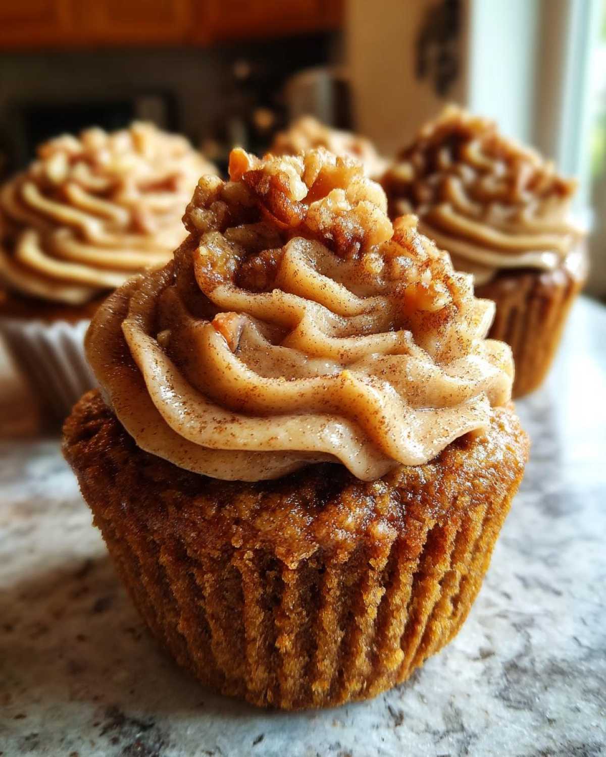 A close-up of a single pecan pie cupcake topped with swirled, cinnamon-dusted frosting and chopped pecans.
