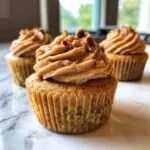 A close-up of freshly baked pecan pie cupcakes topped with brown, swirled frosting and chopped pecans.