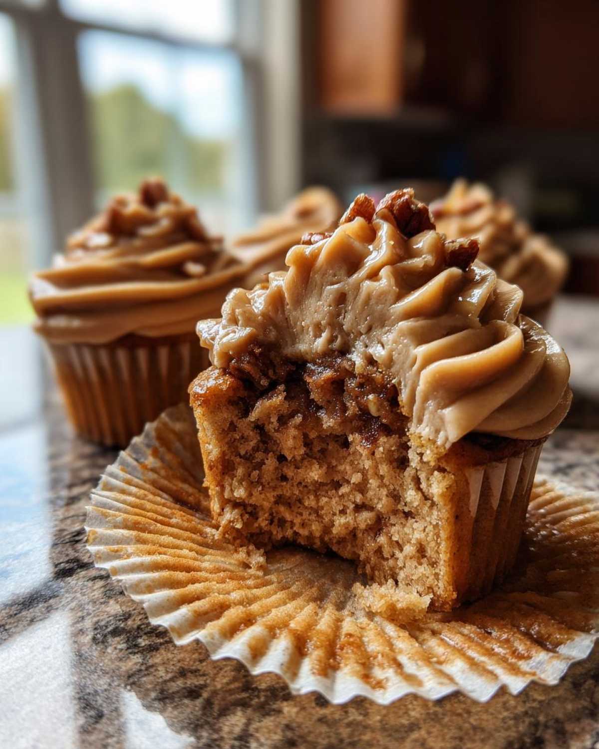 A pecan pie cupcake with a bite taken out, revealing the filling and topped with caramel frosting and pecans.