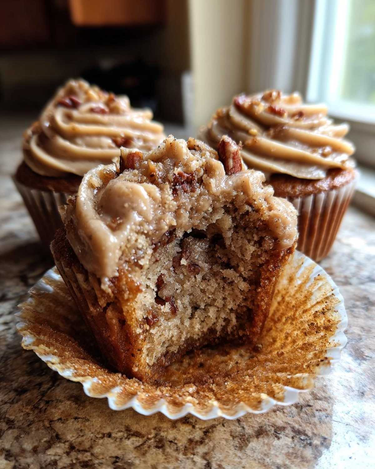Close-up of a pecan pie cupcake cut in half showing the moist interior, topped with brown sugar frosting and pecans.
