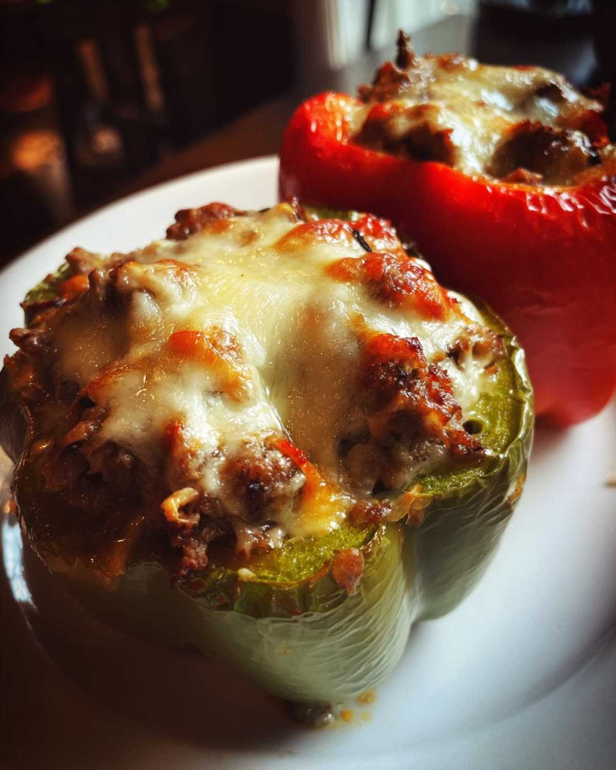 Close-up of a green philly cheesesteak stuffed pepper topped with melted, browned cheese next to a red one.
