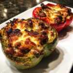 Close-up of baked philly cheesesteak stuffed peppers, featuring a green pepper and a red pepper topped with browned, melted cheese.