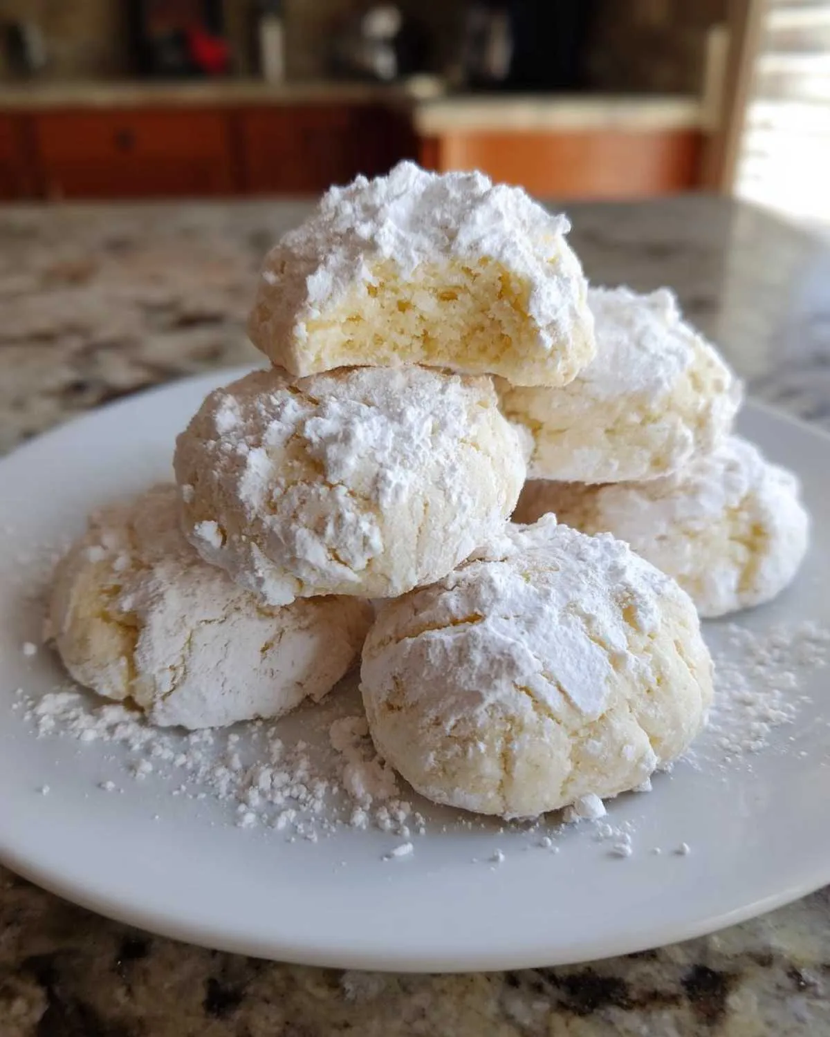 A stack of soft, powdered sugar-dusted cool whip cookies on a white plate, one cookie is broken open.