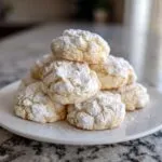 A stack of soft, crinkle-top cool whip cookies heavily dusted with powdered sugar on a white plate.