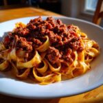 A close-up of fresh pappardelle pasta generously topped with rich, slow-cooked bolognese sauce.