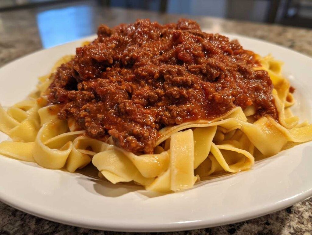 A close-up of a white plate piled high with fresh pasta topped generously with rich, thick bolognese sauce.