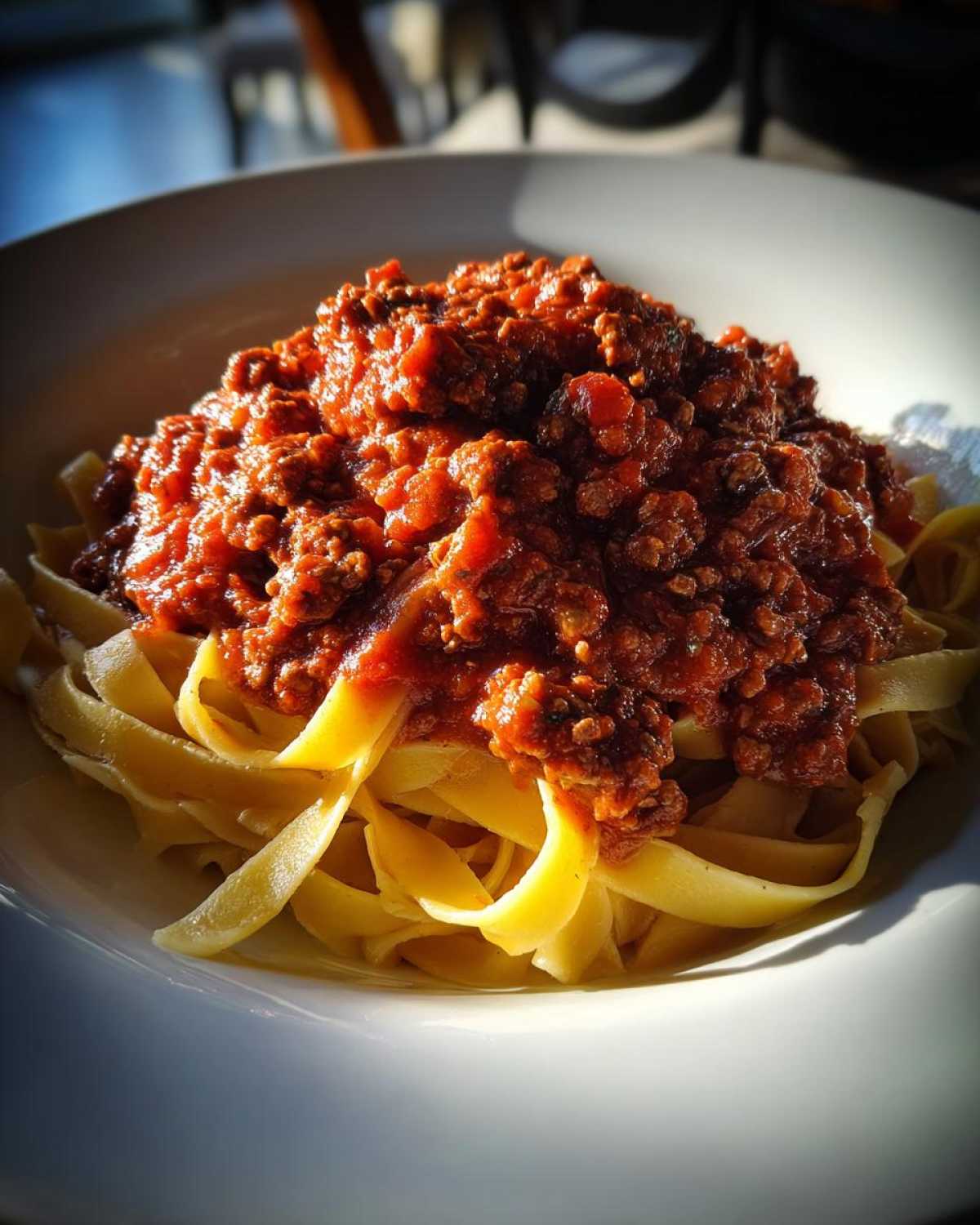 A close-up of fresh tagliatelle pasta generously topped with rich, slow-cooked bolognese sauce.